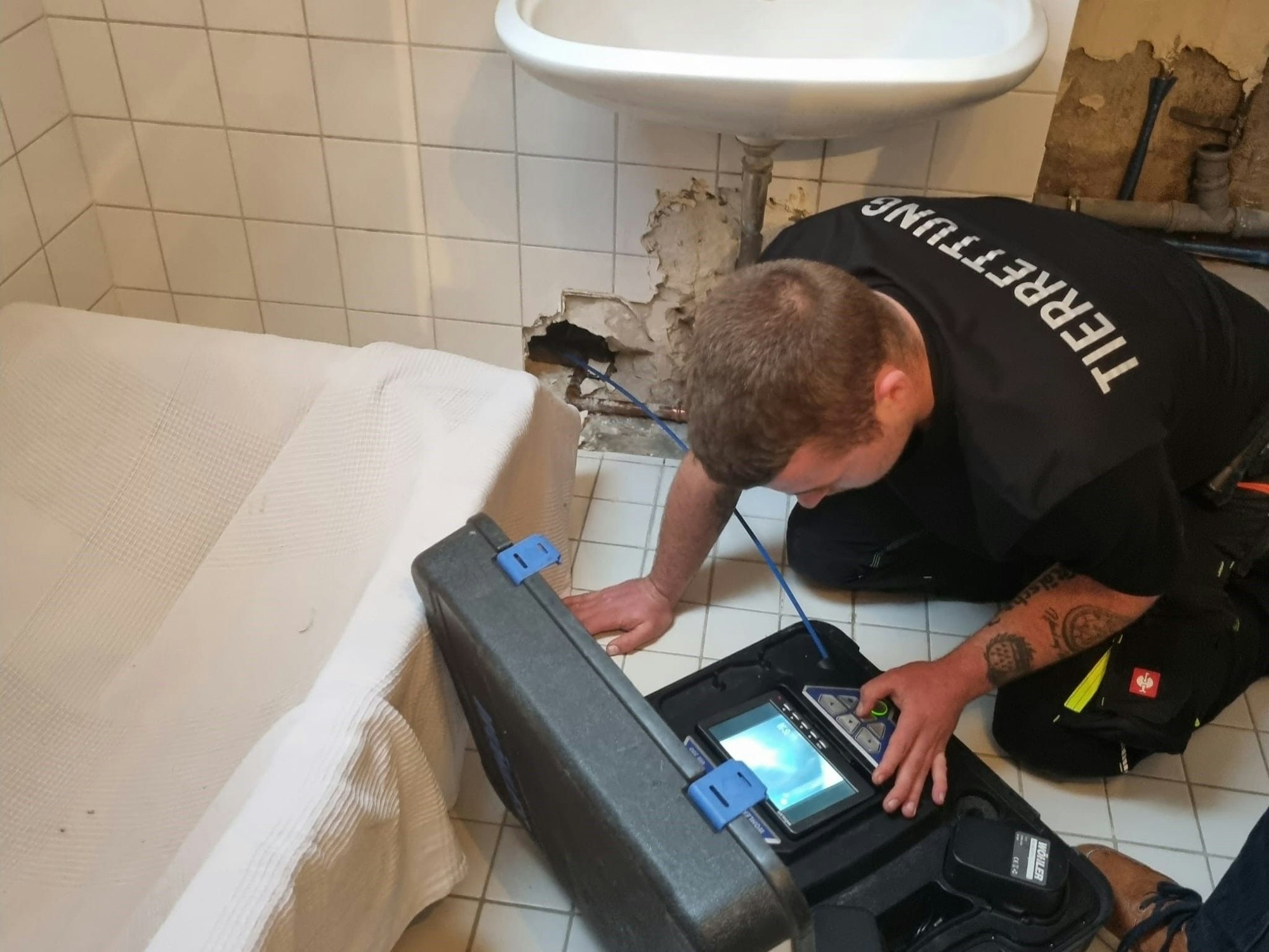 Jordan Wieland von den Tierrettern Köln-Porz kniet auf dem Badezimmerboden und starrt auf einen Bildschirm.