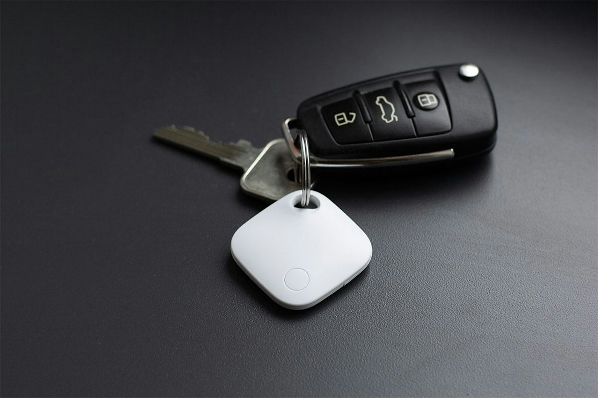 Aldi Smart Tag in Weiß hängt am Autoschlüssel und liegt auf dem Tisch.