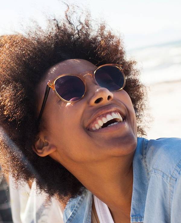 Frau mit Sonnenbrille lacht am Meer