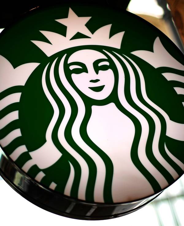 Das Logo der US-amerikanischen Café-Kette Starbucks leuchtet in einem Café.