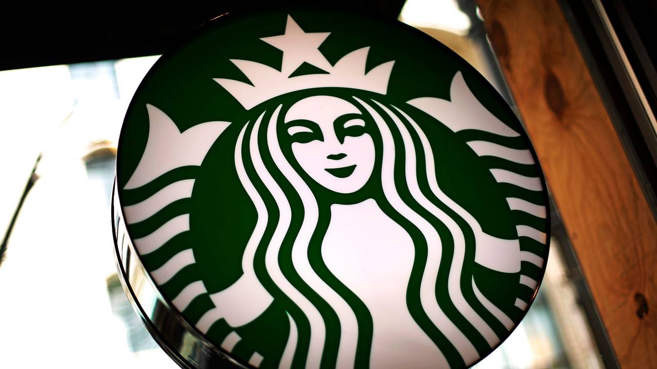 Das Logo der US-amerikanischen Café-Kette Starbucks leuchtet in einem Café.