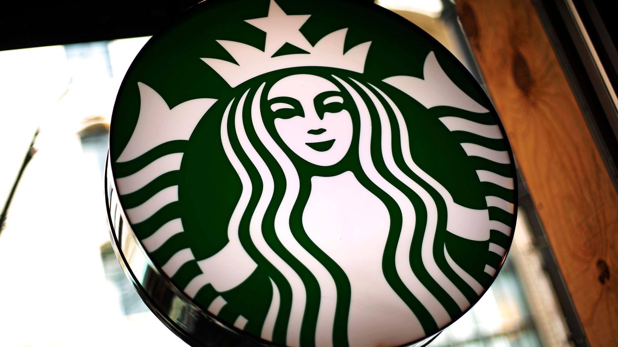 Das Logo der US-amerikanischen Café-Kette Starbucks leuchtet in einem Café.