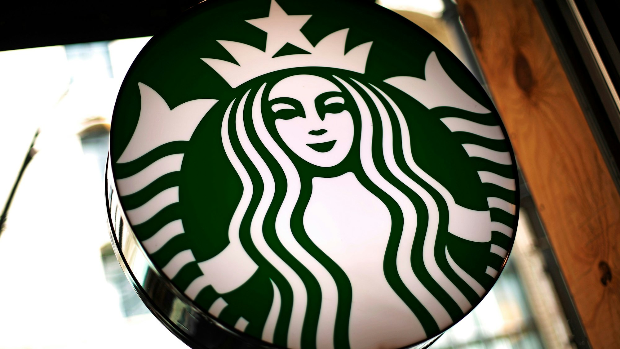 Das Logo der US-amerikanischen Café-Kette Starbucks leuchtet in einem Café.