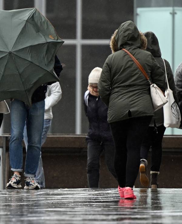 Spaziergänger kämpfen auf der Domplatte mit ihrem Regenschirm (Archivbild vom April 2022): Nach einem freundlichen Vormittag soll es am Sonntagnachmittag und -abend in NRW laut Vorhersage ungemütlich werden.