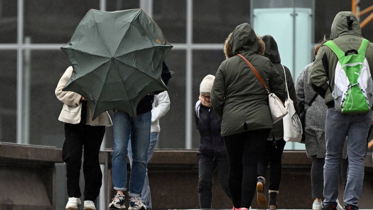 Spaziergänger kämpfen auf der Domplatte mit ihrem Regenschirm (Archivbild vom April 2022): Nach einem freundlichen Vormittag soll es am Sonntagnachmittag und -abend in NRW laut Vorhersage ungemütlich werden.