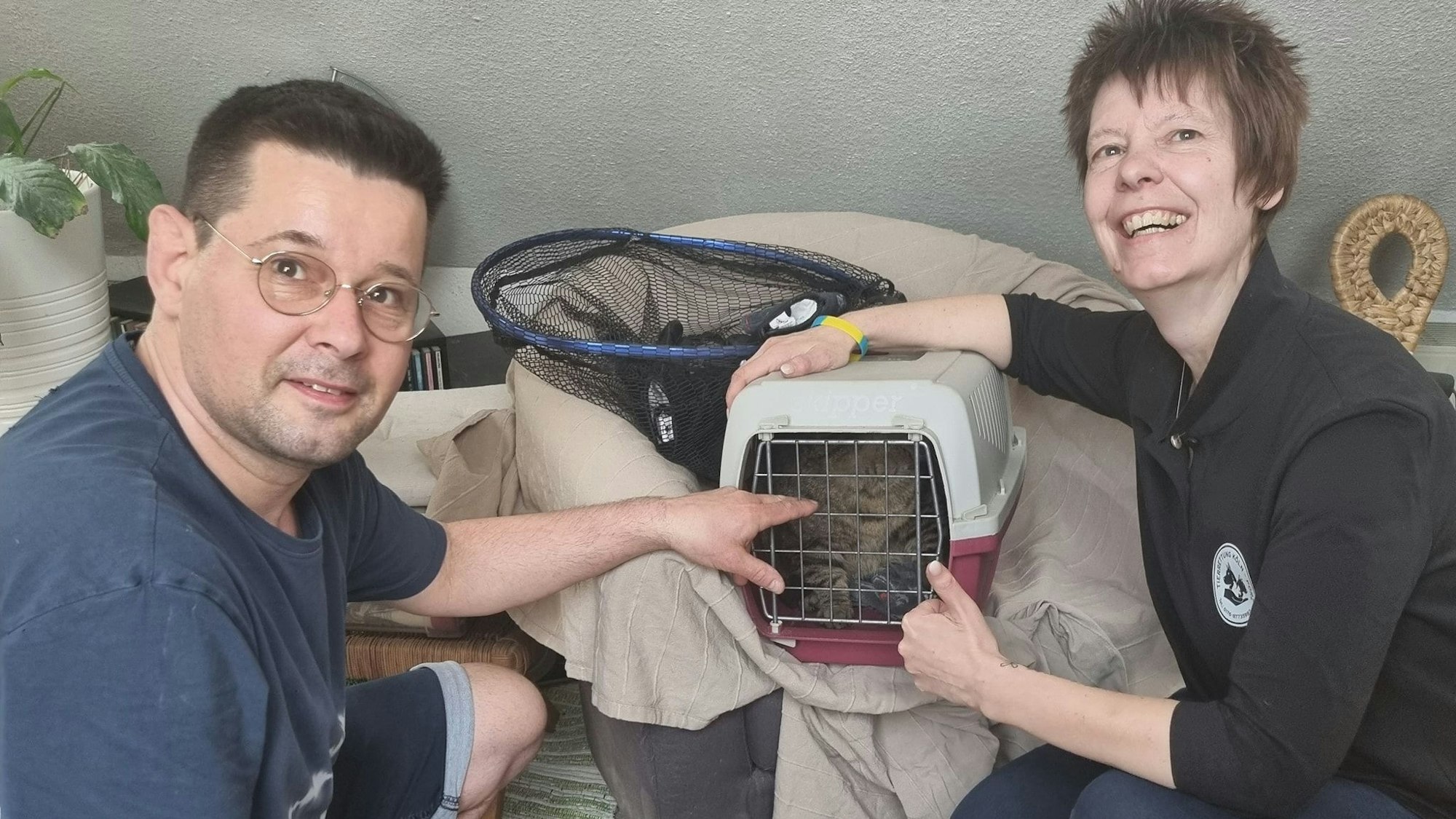 Jörn Schwarz und Antje Sommer von der Tierrettung Köln-Porz hocken neben einer Tierbox, in der sich Kater „Barney“ befindet.