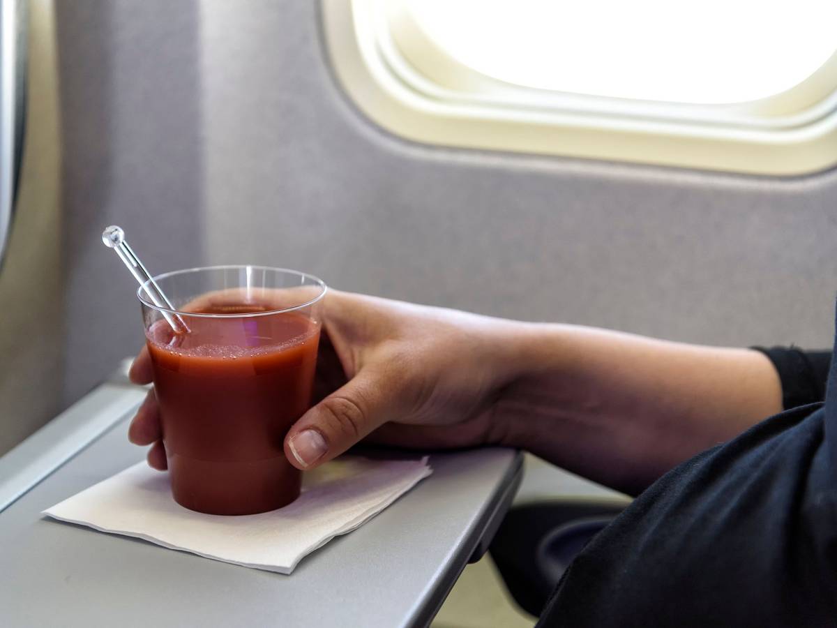 Eine Frau trink ein Glas Tomatensaft im Flugzeug.