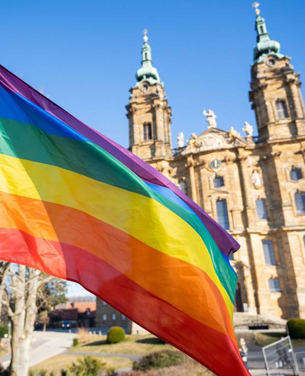 Eine Regenbogenfahne weht vor einer Basilika.