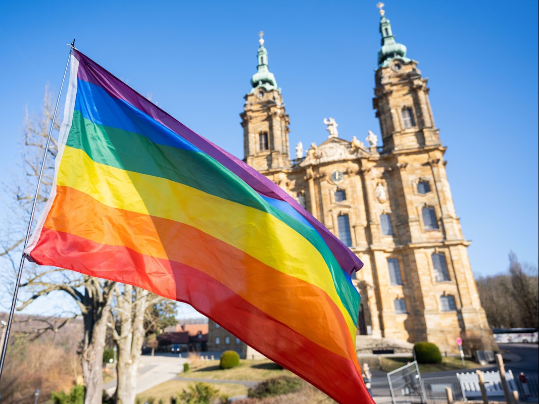 Eine Regenbogenfahne weht vor einer Basilika.