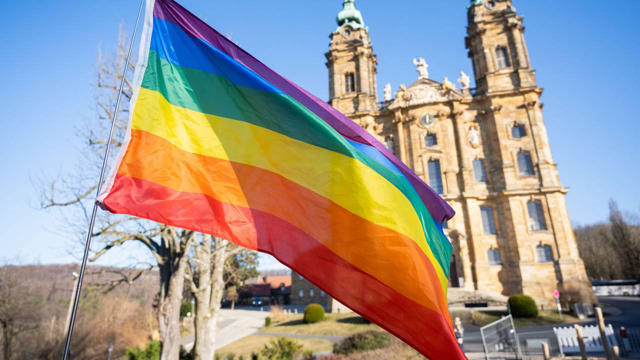 Eine Regenbogenfahne weht vor einer Basilika.