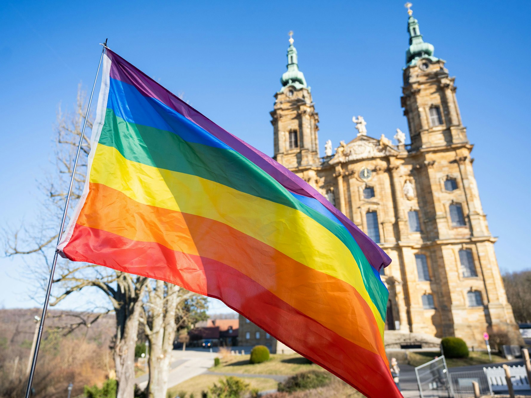 Eine Regenbogenfahne weht vor einer Basilika.