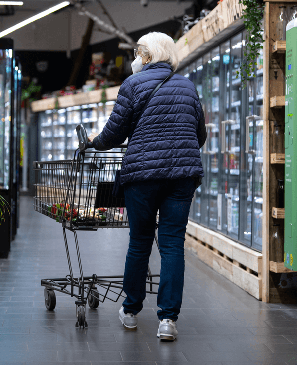 Eine Frau geht mit ihrem Einkaufswagen durch einen Supermarkt.