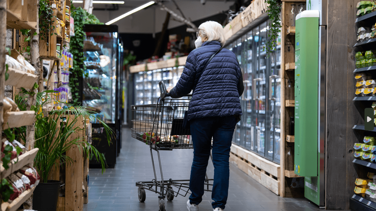 Eine Frau geht mit ihrem Einkaufswagen durch einen Supermarkt.