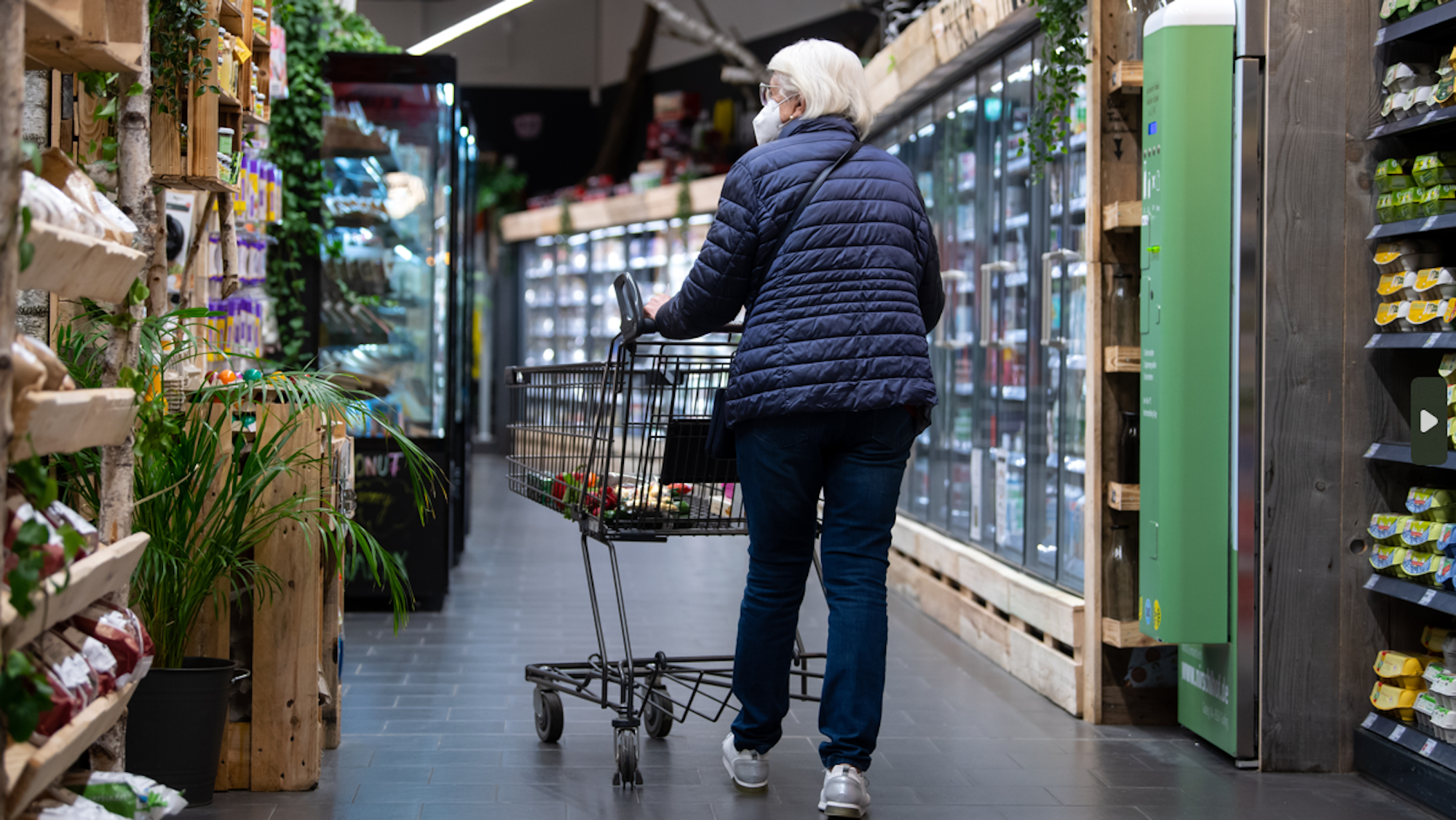 Eine Frau geht mit ihrem Einkaufswagen durch einen Supermarkt.