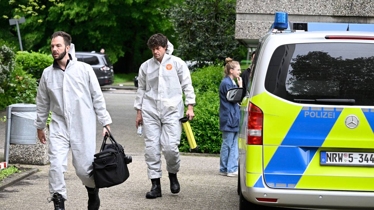 Zwei Beamte der Spurensicherung sind in Schutzanzügen auf dem Weg zu einem Tatort, dabei laufen sie an einem Polizeifahrzeug vorbei.