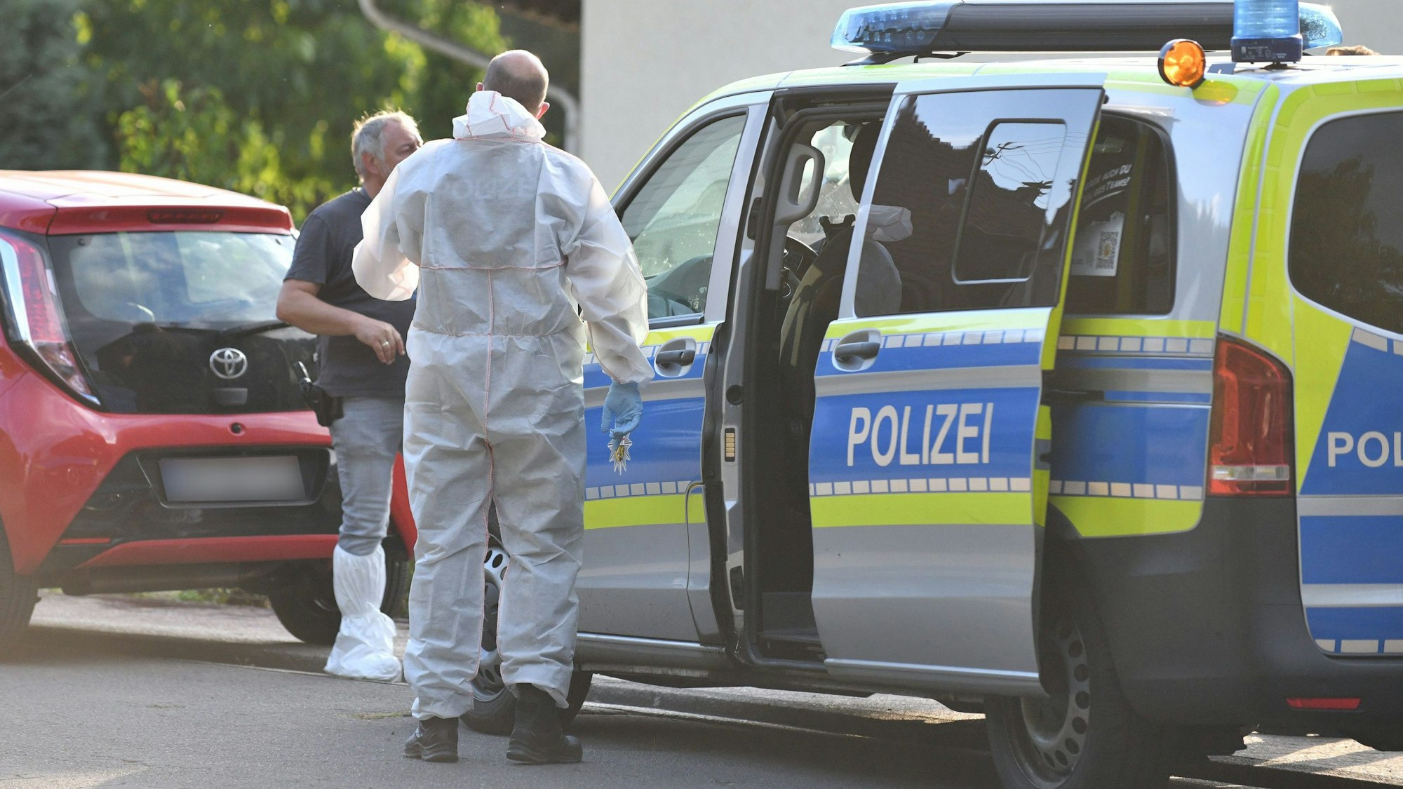 Einsatzkräfte der Polizei und Spurensicherung stehen vor einem Haus.