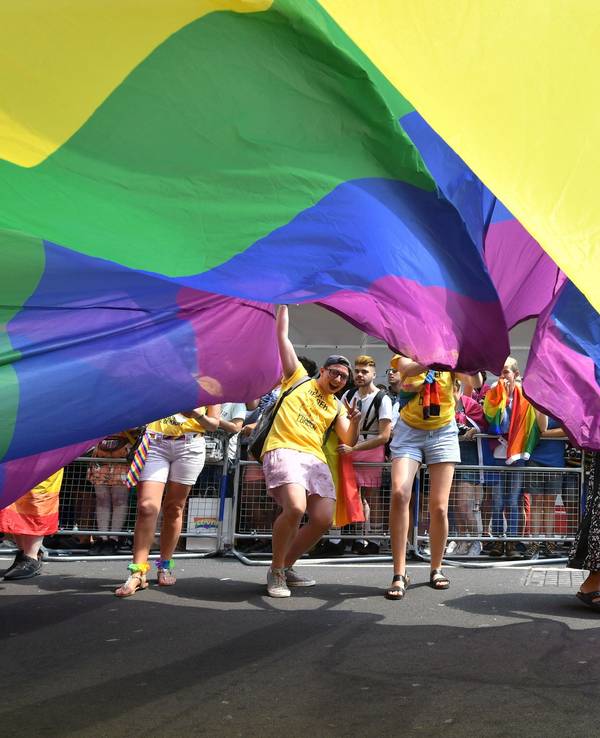 Teilnehmende der Londoner Pride Parade 2018 schauen unter einer riesigen Regenbogenflagge hervor.