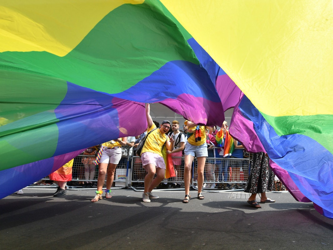 Teilnehmende der Londoner Pride Parade 2018 schauen unter einer riesigen Regenbogenflagge hervor.