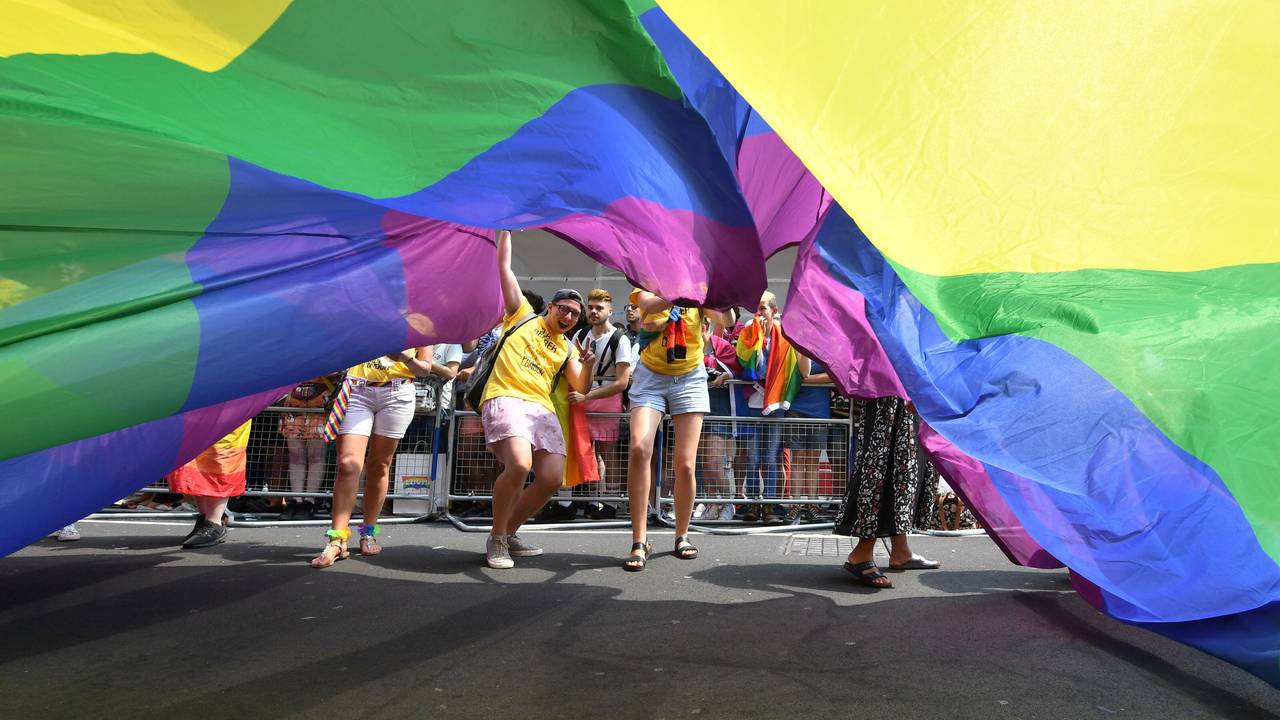 Teilnehmende der Londoner Pride Parade 2018 schauen unter einer riesigen Regenbogenflagge hervor.