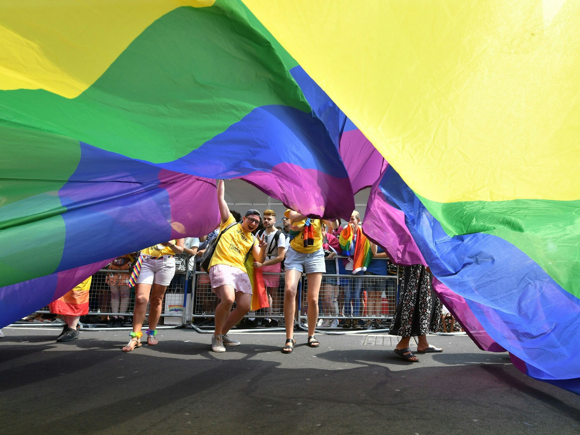 Teilnehmende der Londoner Pride Parade 2018 schauen unter einer riesigen Regenbogenflagge hervor.
