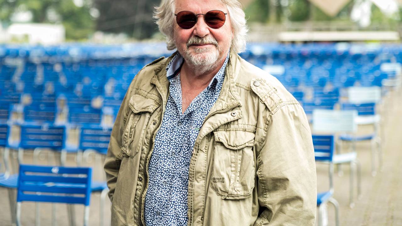 Tommy Engel steht mit Sonnenbrille im Tanzbrunnen vor leeren blauen Stühlen.