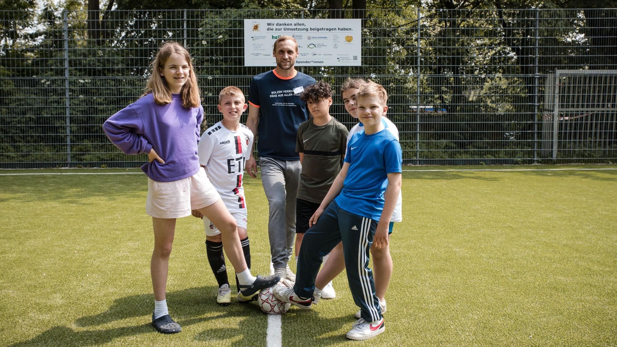 Marcel Risse posiert mit Kindern auf dem neuen Kunstrasenplatz in Köln.