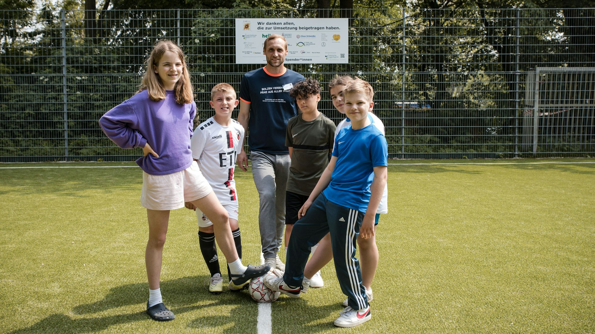 Marcel Risse posiert mit Kindern auf dem neuen Kunstrasenplatz in Köln.