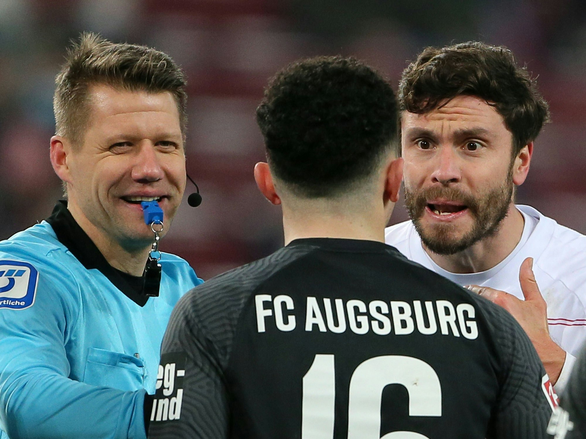 FC-Kapitän Jonas Hector während einer Auseinandersetzung mit Augsburgs Ruben Vargas und Schiedsrichter Patrick Ittrich.