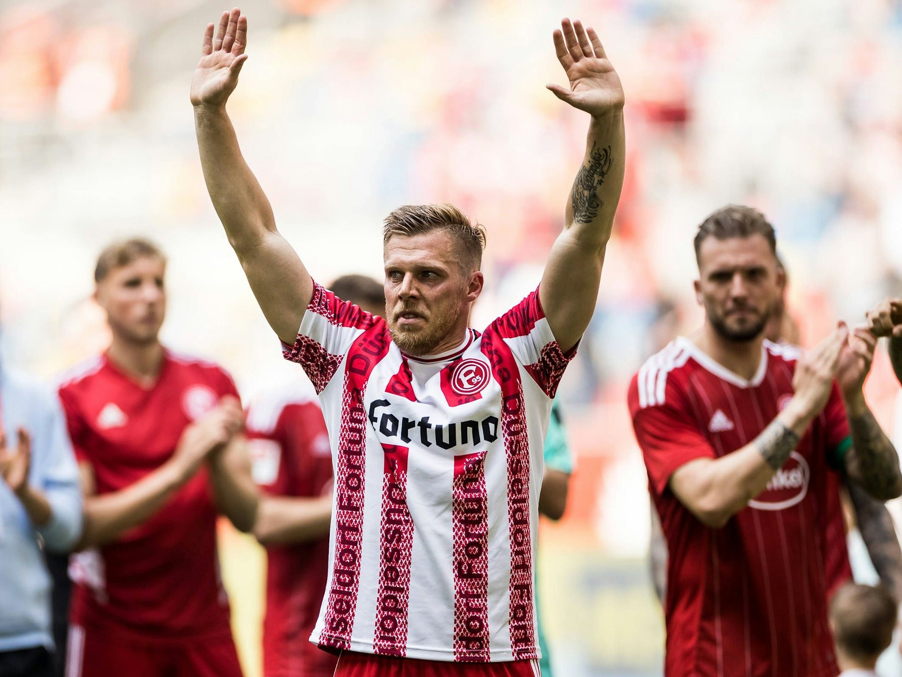 Rouwen Hennings steht im Stadion und reckt die Arme in die Höhe.