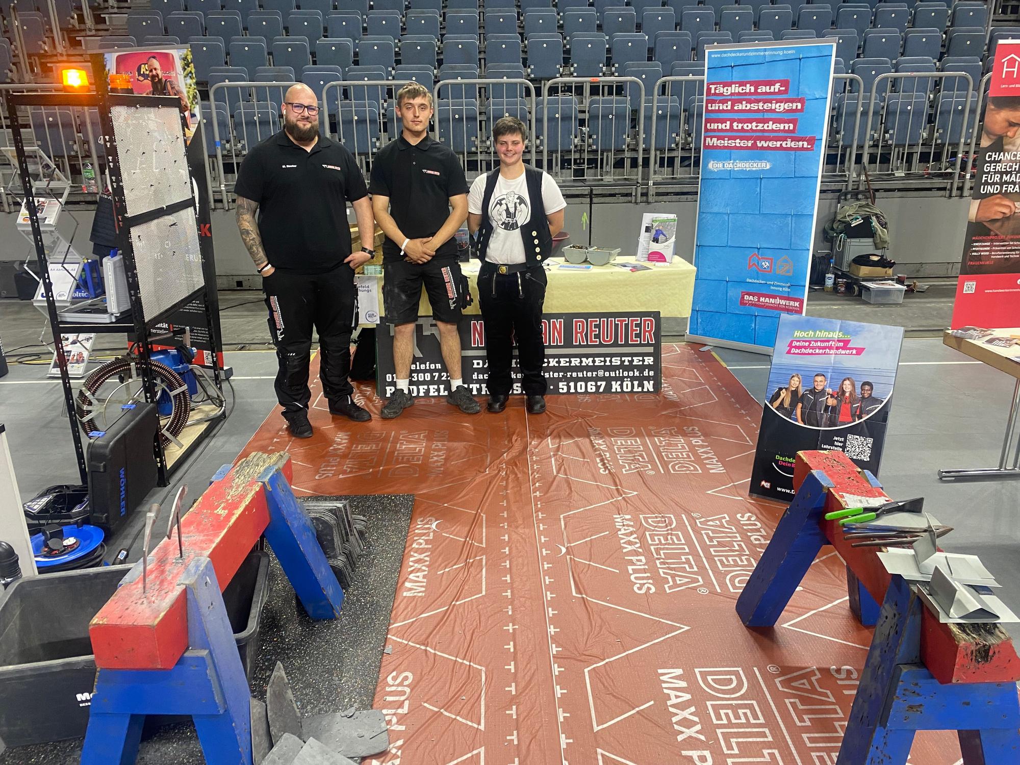 Norman Reuter steht mit einem Kollegen und einer Kollegin an seinem Stand in der Lanxess-Arena
