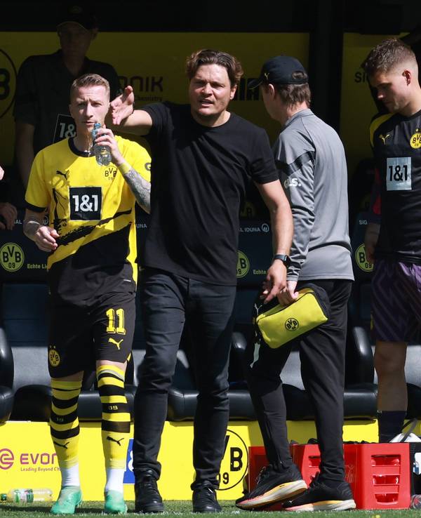Sebastian Kehl, Marco Reus und Edin Terzic stehen an der Seitenlinie. Reus trinkt aus einer Wasserflasche, Kehl und Terzic gestikulieren.