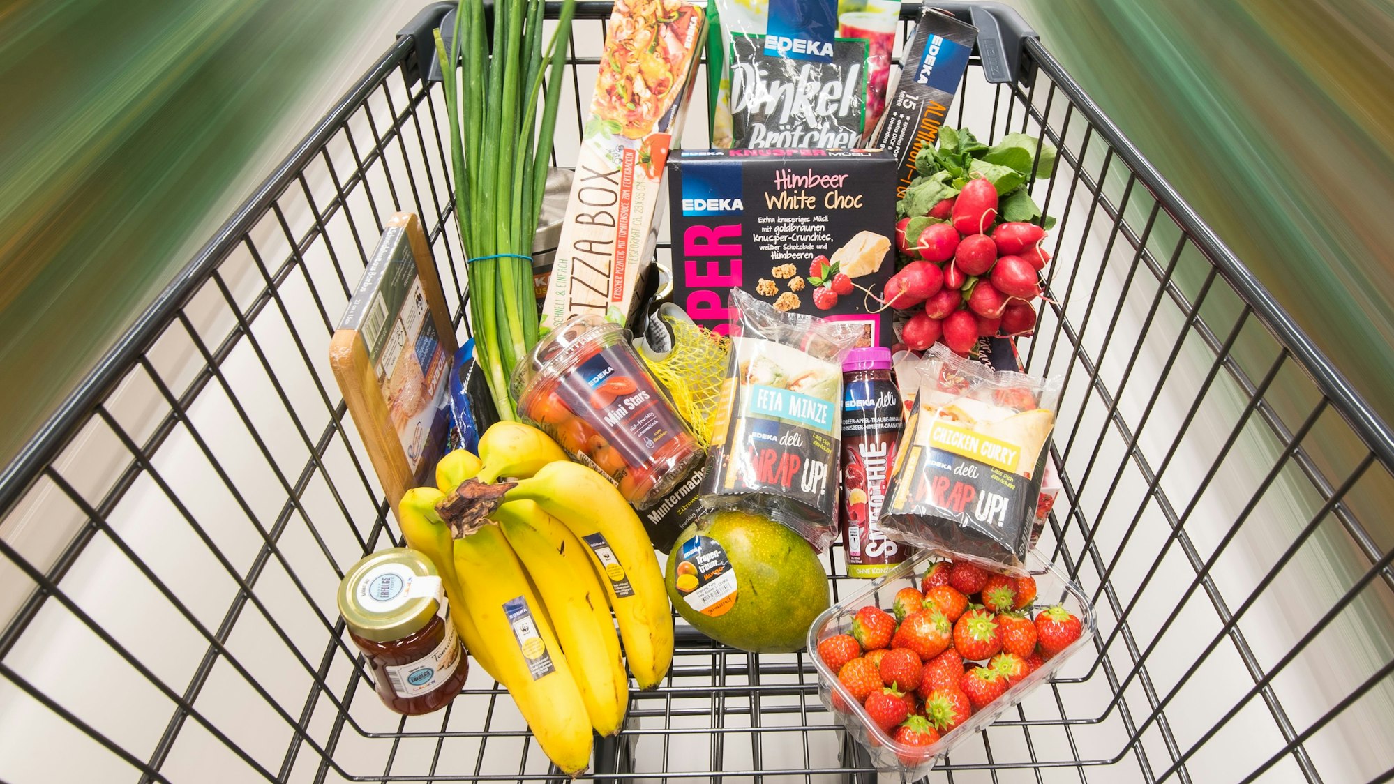 Ein Einkaufswagen mit Edeka-Produkten wird durch einen Supermarkt geschoben