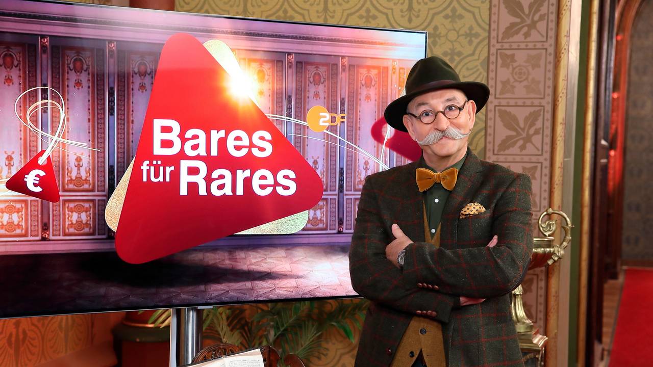 Moderator Horst Lichter steht neben dem Logo der Sendung „Bares für Rares“-