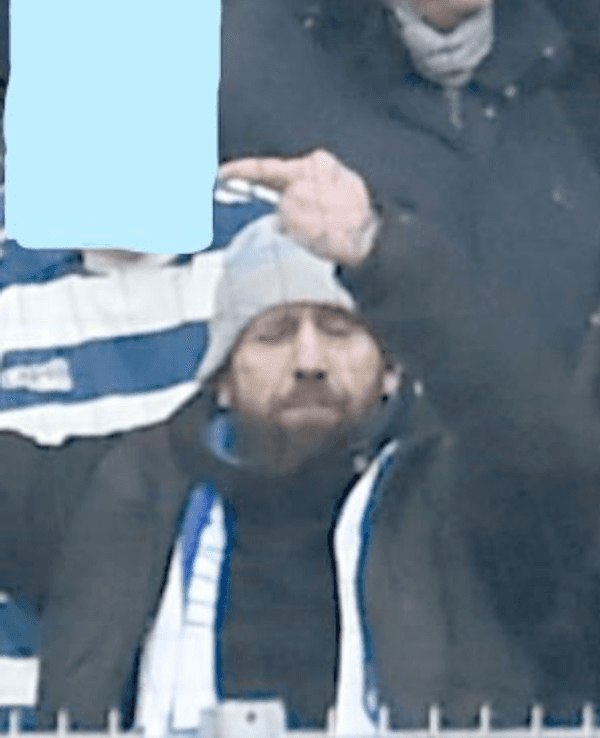 Ein Mann, mit Schal und Mütze bekleidet, steht auf einer Tribüne.