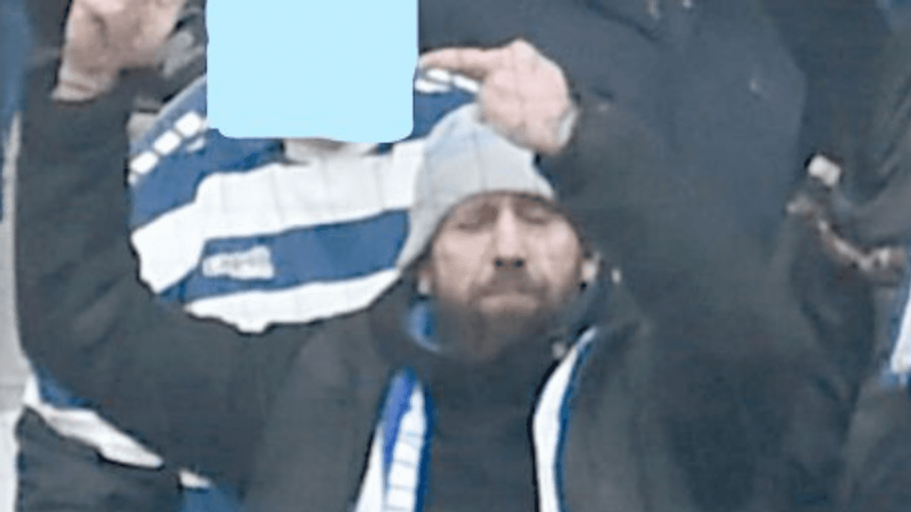 Ein Mann, mit Schal und Mütze bekleidet, steht auf einer Tribüne.