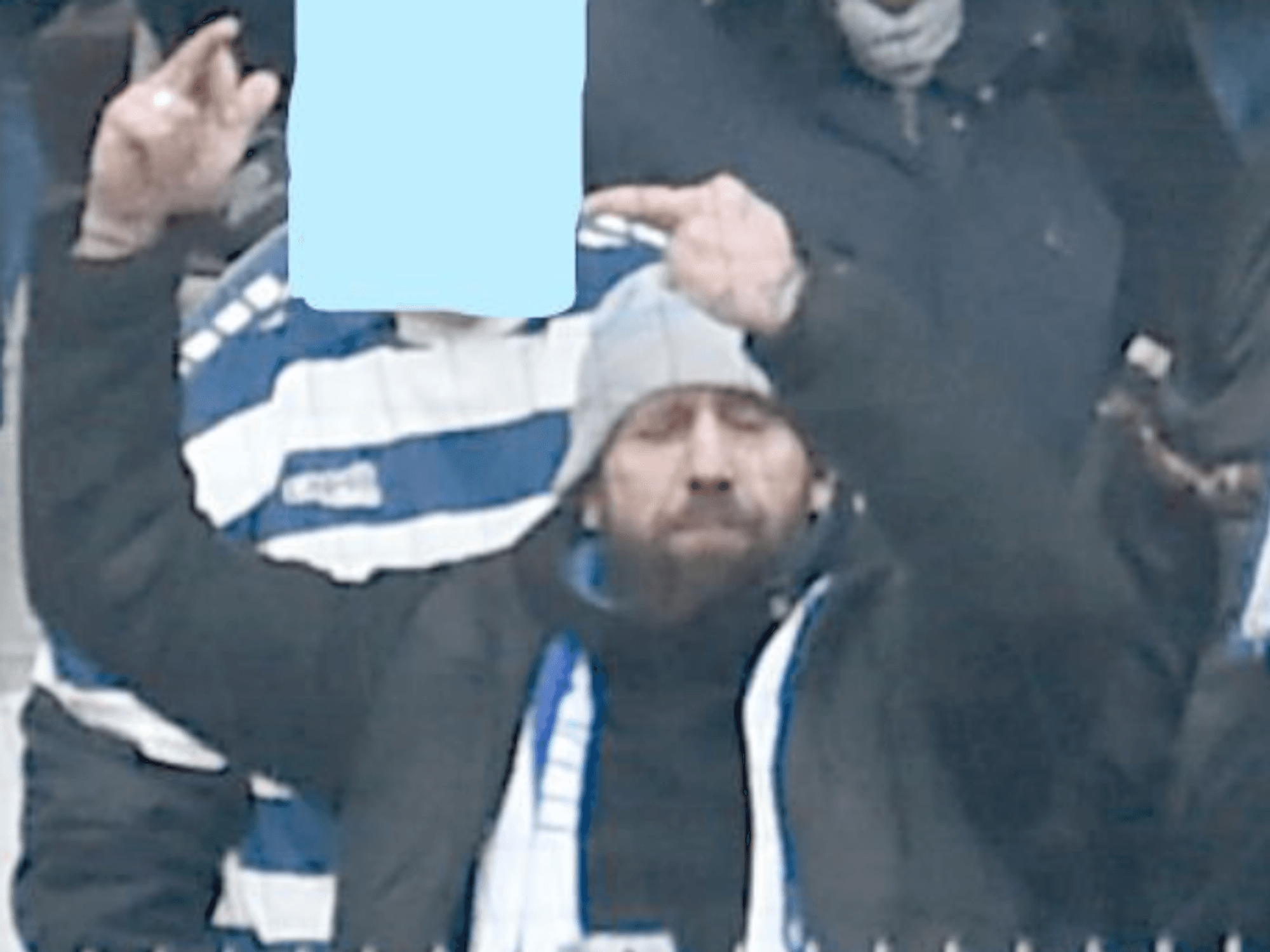Ein Mann, mit Schal und Mütze bekleidet, steht auf einer Tribüne.