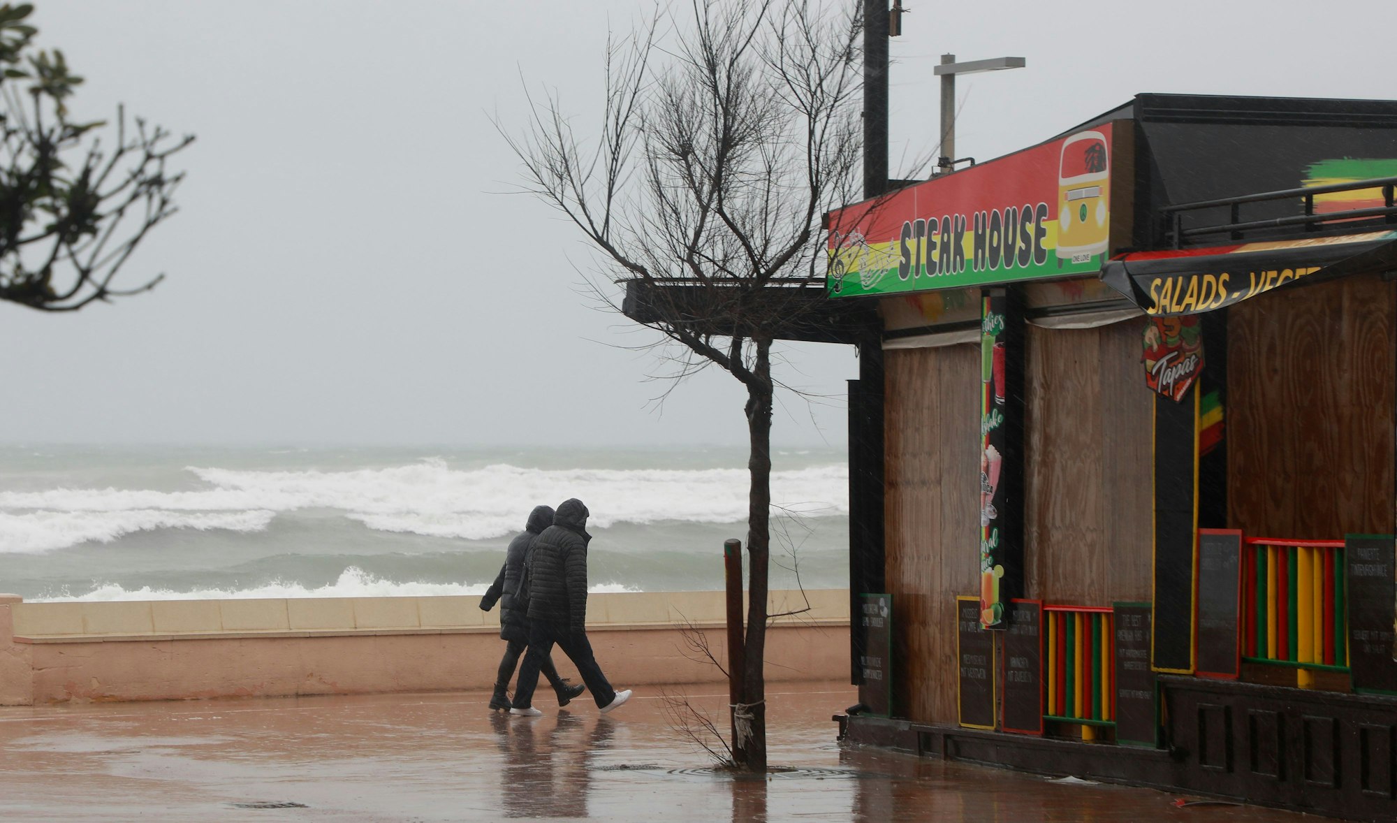 Ein Paar geht bei stürmischem Wetter an der Strandpromenade von Can Picafort spazieren.