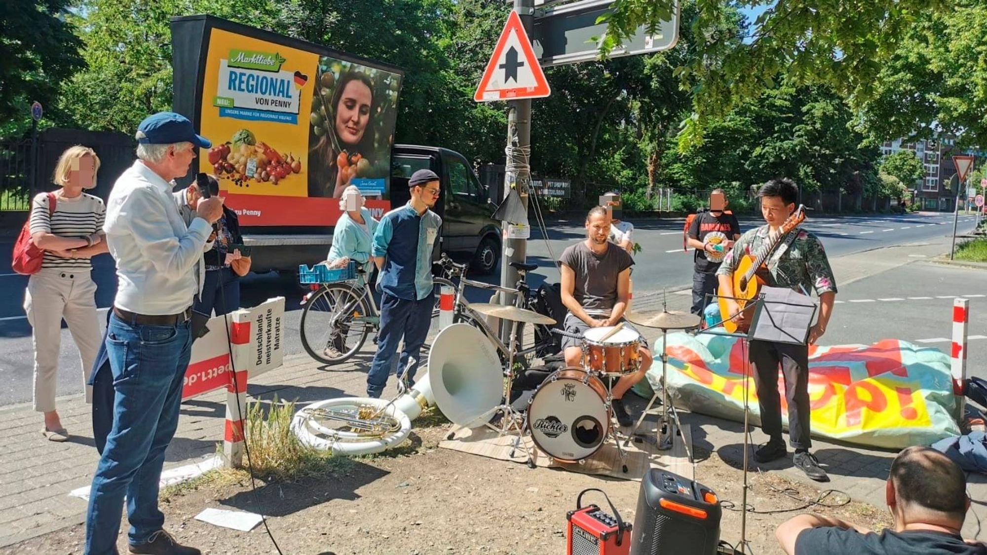 Eine Band spielt am Gehweg vor dem OMZ-Haus, dabei steht ein Mann mit Mikrofon. Eine handvoll Passantinnen und Passanten sind stehen geblieben.
