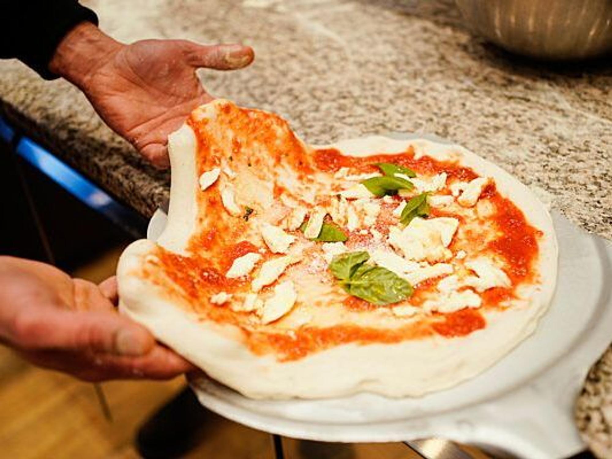 Eine Pizza Margherita wird für den Ofen vorbereitet.