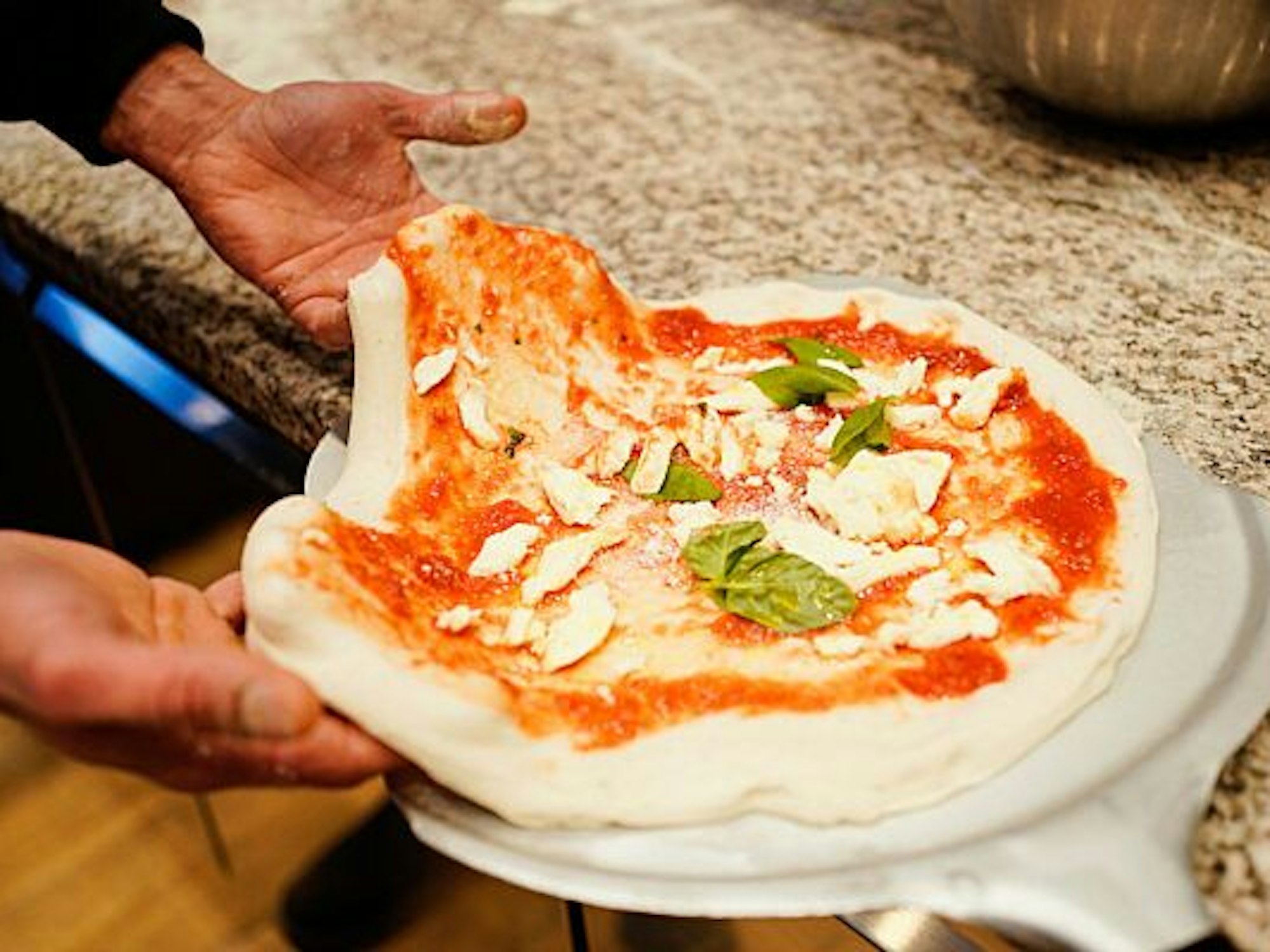 Eine Pizza Margherita wird für den Ofen vorbereitet.