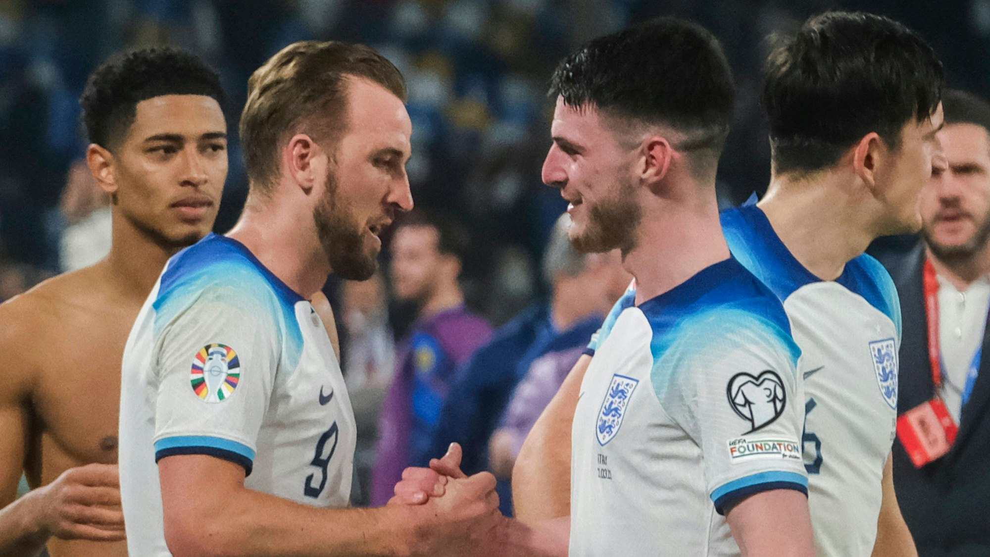 Harry Kane und Declan Rice schlagen im Trikot der englischen Nationalmannschaft miteinander ein. Im Hintergrund ist Jude Bellingham zu sehen.