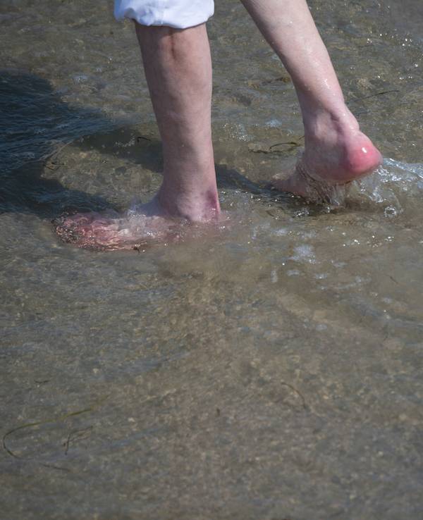 Ein Mann watet durch das flache Wasser am Strand des Seebads. Viele Ostseebäder machen derzeit mit Aushängen auf die Gefahr durch Vibrionen aufmerksam.