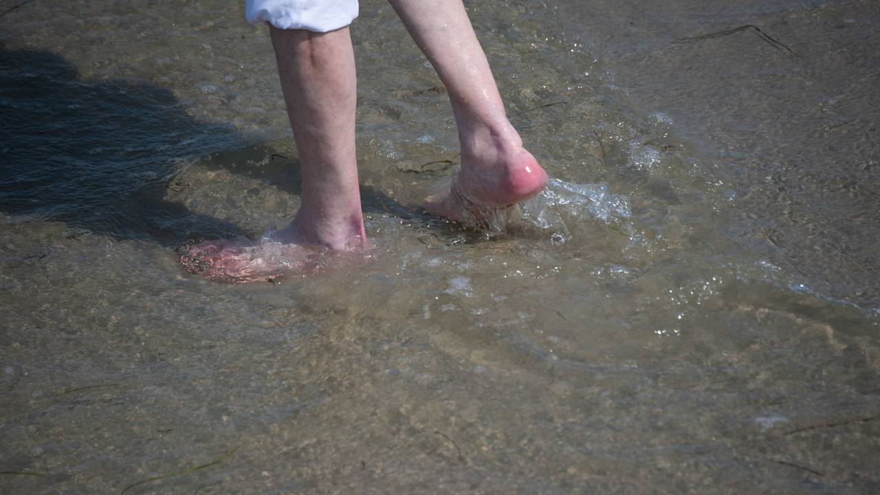 Ein Mann watet durch das flache Wasser am Strand des Seebads. Viele Ostseebäder machen derzeit mit Aushängen auf die Gefahr durch Vibrionen aufmerksam.