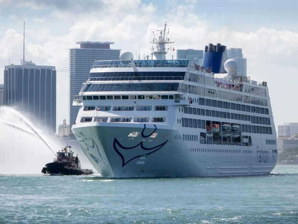 Ein Kreuzfahrtschiff auf dem Meer, im Hintergrund Wolkenkratzer.