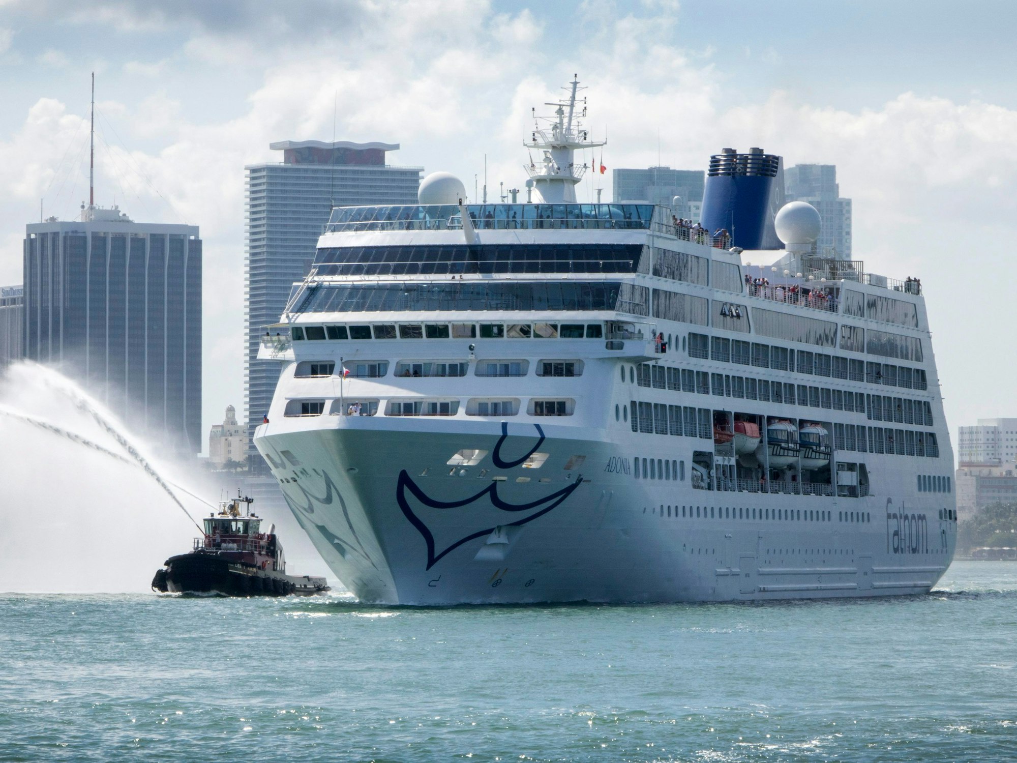 Ein Kreuzfahrtschiff auf dem Meer, im Hintergrund Wolkenkratzer.