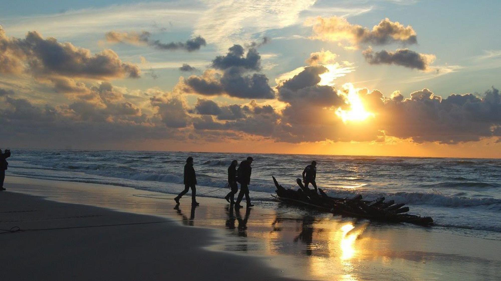 Menschen gehen im Sonnenuntergang am Strand entlang.