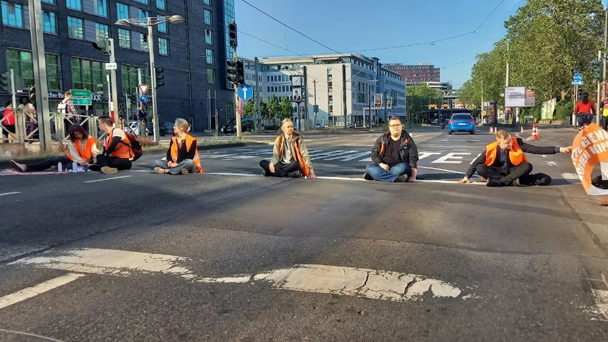 Sechs Menschen sitzen bei einem Protest in Köln-Deutz auf der Straße.