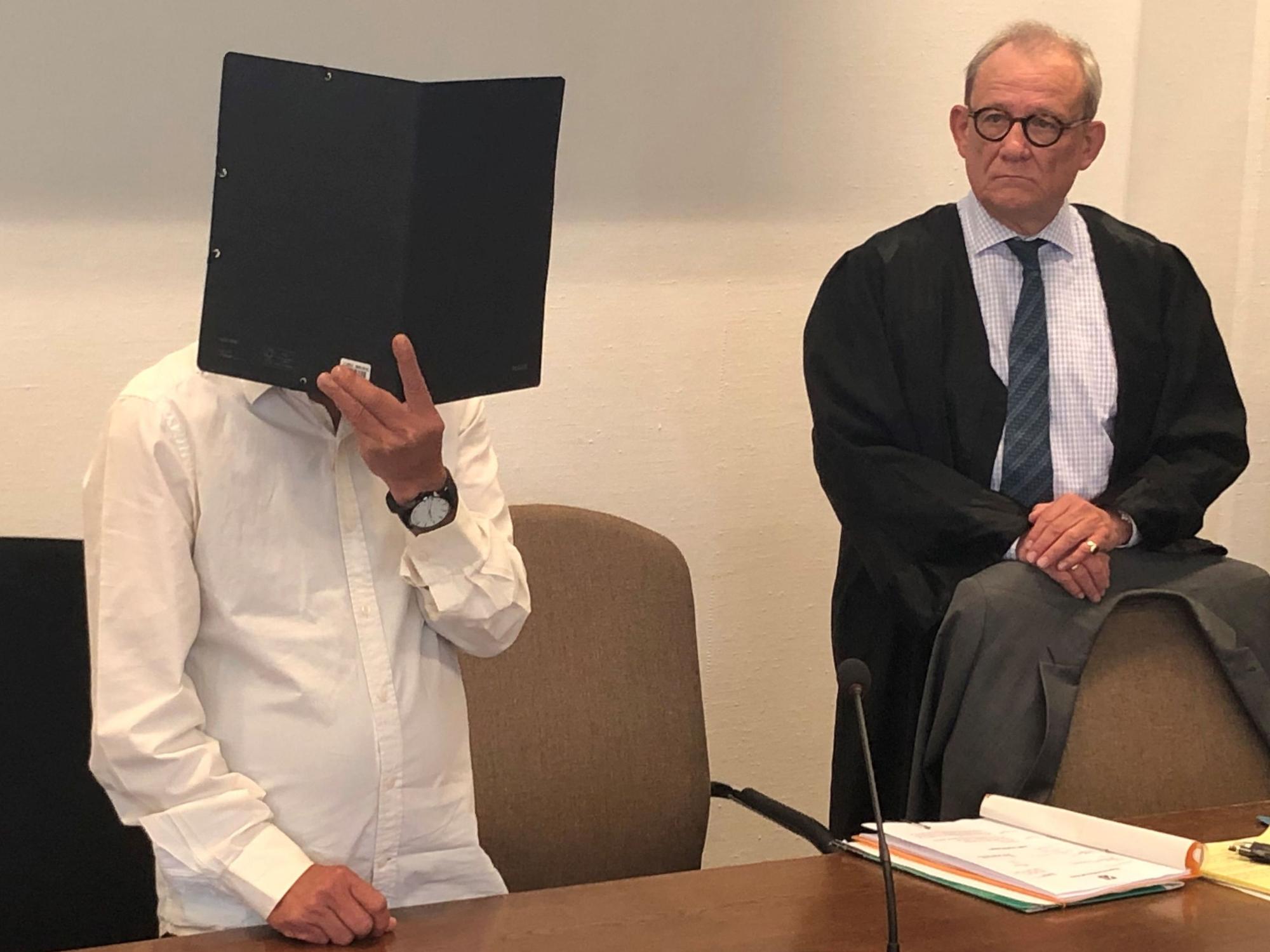 Zum Prozessbeginn in Köln verdeckt der Angeklagte sein Gesicht mit einem Ordner.