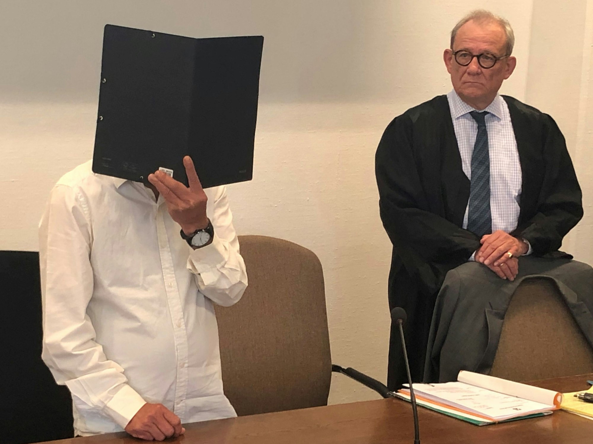 Zum Prozessbeginn in Köln verdeckt der Angeklagte sein Gesicht mit einem Ordner.