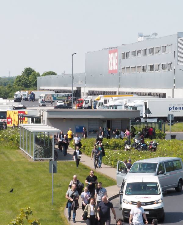 Menschen, Auto und Lkw sind an einem großen Rewe-Gebäude in Köln zu sehen.